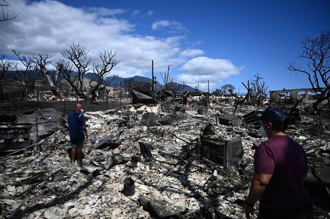 내 집은 어디에… - 지난 11일(현지 시각) 미국 하와이주 마우이섬의 라하이나 지역에서 주민들이 화재로 폐허가 된 마을을 둘러보고 있다. 지난 8일 발생한 산불로 마을 건물들이 잿더미로 변했다. 13일 미국 언론들은 이번 화재로 실종된 인원이 수백~1000여 명에 이를 것으로 예상된다고 보도했다. /AFP 연합뉴스