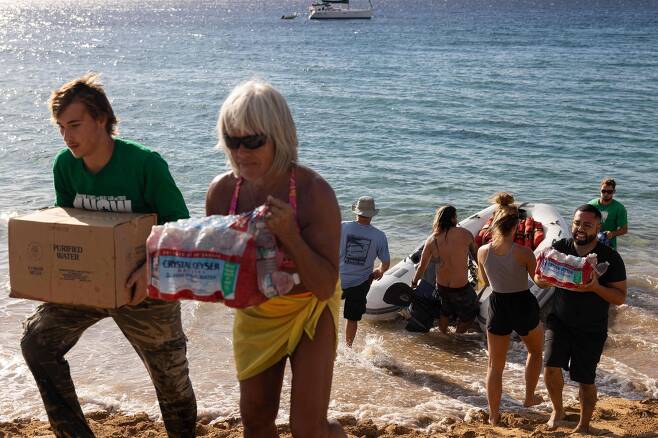 자원봉사자들이 8월 12일 하와이주 마우이섬 서부 라하이나의 블랙 록 비치에서 산불로 주택과 사업장이 파괴된 서부 마우이 한 마을에 지원 물품을 내리고 있다./AFP 연합뉴스