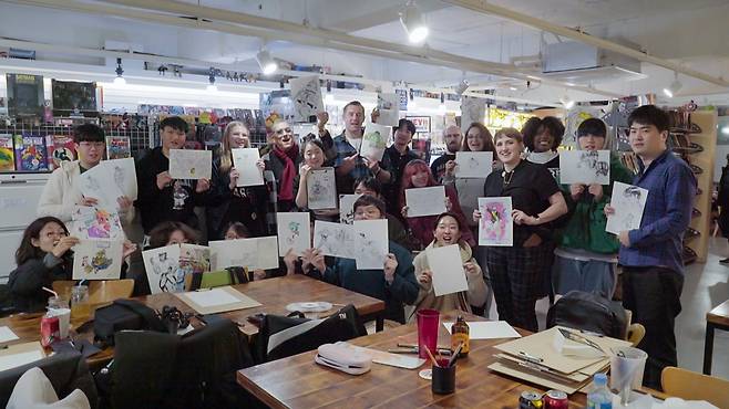 Guests holding up their drawings from a "Drink & Draw" event under the theme of "Life In Korea." The Drink & Draw event is hosted by Dice and Comics Cafe every Thursday. (The Korea Herald)