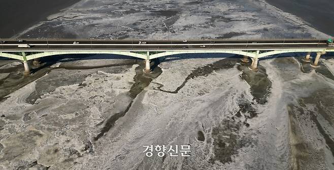 차들이 얼어있는 한강 위에 서 있는 일산대교 위를 지나가고 있다.