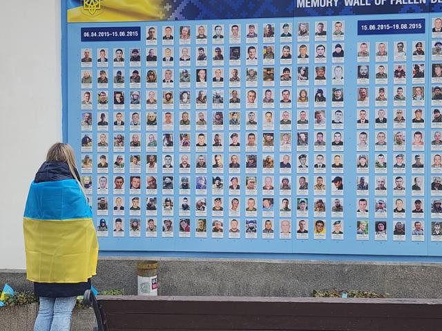 러시아의 우크라이나 침공 2년을 맞은 24일 우크라이나 수도 키이우 '추모의 벽' 앞에서 우크라이나 국기를 몸에 두른 한 여성이 전사자 명단을 바라보고 있다. 성 미카엘 대성당을 둘러싼 추모의 벽에는 러시아군과 싸우다 목숨을 잃은 우크라이나 군인들의 사진이 빼곡하게 붙어 있다. 키이우=신은별 특파원