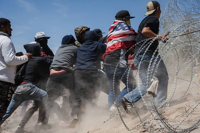 2024년 3월 22일 한 무리의 이민자들이 미국 텍사스주 엘패소 근처 미국-멕시코 국경에서 철조망을 뚫고 국경을 넘으려고 시도하고 있다. /로이터 연합뉴스