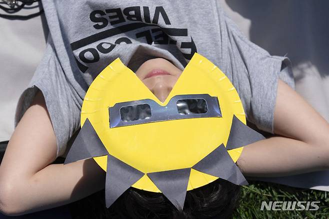 [워싱턴=AP/뉴시스] 8일(현지시각) 미 워싱턴 내셔널 몰에서 관측경을 착용한 소년이 편하게 누워 달이 태양을 완전히 가리는 개기일식을 관측하고 있다. 2024.04.09.