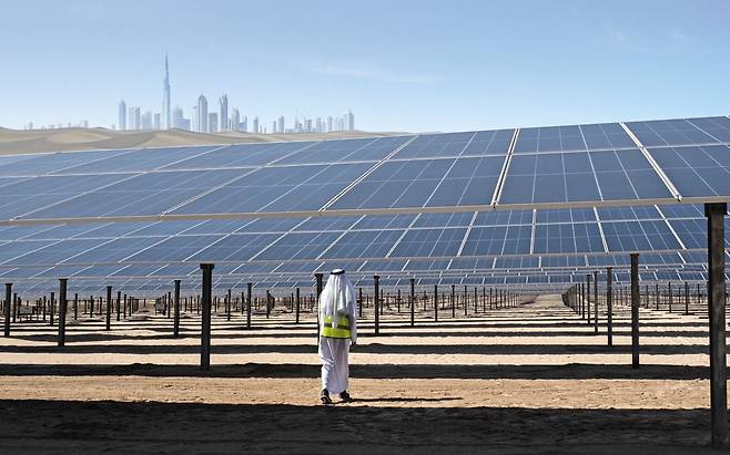 아랍에미리트(UAE) 아부다비의 ‘알 다프라’ 태양광 발전소를 향해 전통 복장인 칸도라 차림의 남성이 발걸음을 옮기고 있다. 태양광 패널 400만 개를 갖춘 알 다프라는 발전 용량만 2기가와트(GW)로, 탄소 배출을 연간 240만t 줄이는 효과가 있다. UAE는 2030년까지 전체 전력 생산량의 25%를 재생에너지로 채우겠다는 목표다. 사진 왼쪽 위 도심은 그래픽 처리한 두바이의 스카이라인. /사진=게티이미지코리아, 그래픽=김의균