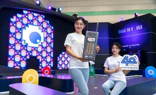 SK텔레콤 모델이 17일 서울 강남구 코엑스에서 개최된 '2024 월드 IT쇼' SK텔레콤 전시장에서 국내 최초의 무선전화 서비스 카폰(차량 전화) 모형을 든 가운데 뒤쪽으로 인공지능(AI) 비서 서비스 '에이닷' 디자인이 보인다. SK텔레콤 제공