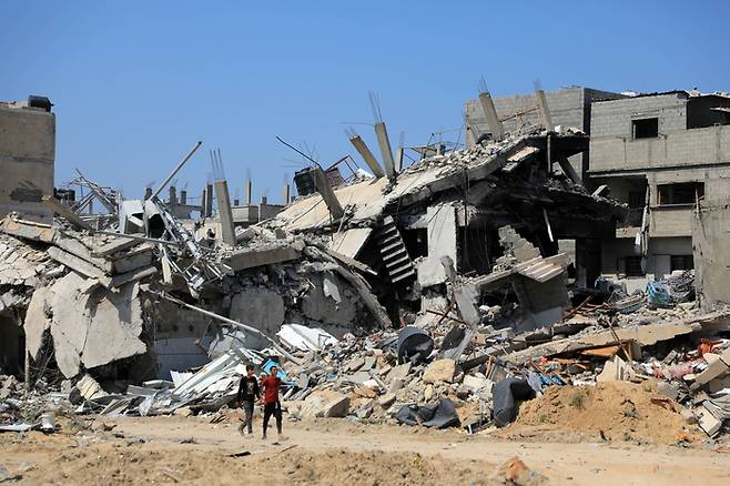 팔레스타인인들이 16일(현지시간) 가자지구 남부 칸유니스의 무너진 건물 앞을 지나가고 있다.  신화연합뉴스