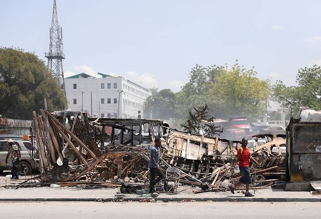 /로이터 연합뉴스지난달 25일 아이티의 수도 포르토프랭스의 대통령 궁 인근에서 갱단의 방화로 불에 탄 차량 앞을 시민들이 지나고 있다.
