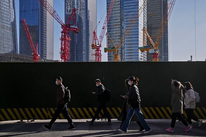 2023년 3월 베이징 중심업무지구의 사무실 건물 근처에서 마스크를 쓴 사람들이 건설 현장 앞을 지나가고 있다. AP 연합뉴스