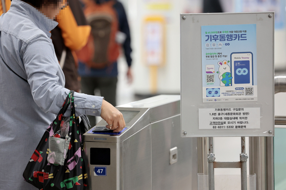 A person passes through the subway turnstiles at the platform at Gwanghwamun Station in central Seoul on April 7, with a banner advertising the Climate Card unlimited public transportation pass displayed nearby. [YONHAP]