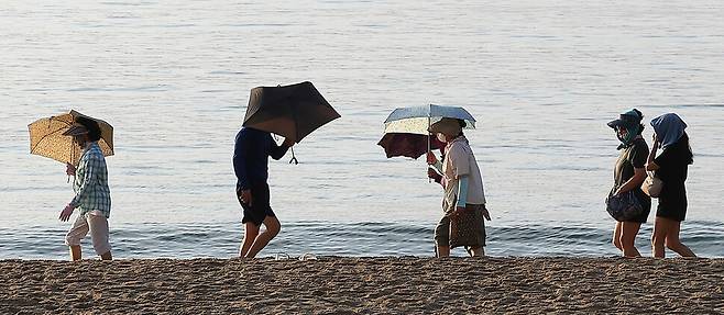 열대야와 무더위가 이어진 19일 오전 부산 수영구 광안리해수욕장에서 시민들이 햇살을 피해 양산과 모자, 가리개 등을 하고 해변 맨발 걷기를 하고 있다. 연합뉴스