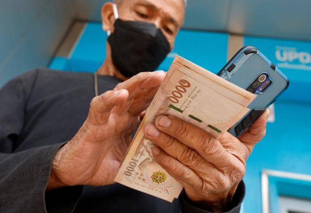 지난 1월 태국 방콕에서 한 시민이 정부의 1만 밧 보조금이 지급되자 이를 현금으로 인출한 뒤 확인하고 있다. 방콕=EPA 연합뉴스