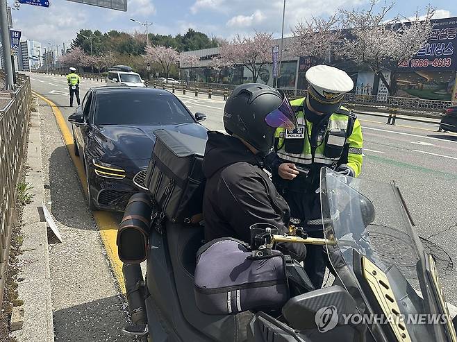 '신호위반 적발' (원주=연합뉴스) 강태현 기자 = 15일 낮 원주 시내 도로에서 40대 오토바이 운전자가 신호위반으로 암행순찰차 단속망에 걸려 범칙금 처분을 받고 있다. 2025.4.15 taetae@yna.co.kr