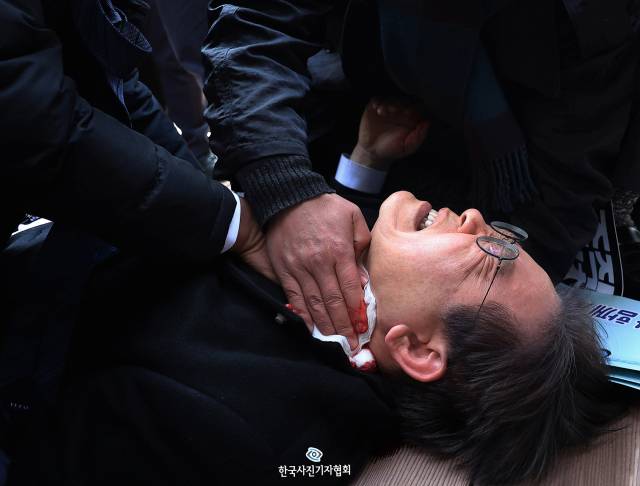 <61회 한국보도사진상 - 최우수상> 더불어민주당 이재명 대표가 2일 오전 부산 강서구 가덕도 신공항 부지 방문을 마친 뒤 이동하던 순간 김모(67)씨에 흉기 습격을 당해 바닥에 쓰러져 고통 스러워하고 있다. 이 대표는 피습 직후 지혈을 하던 당 관계자에게 "더 세게 눌러달라"고 말했다. 사진 제공=한국사진기자협회(KPPA)