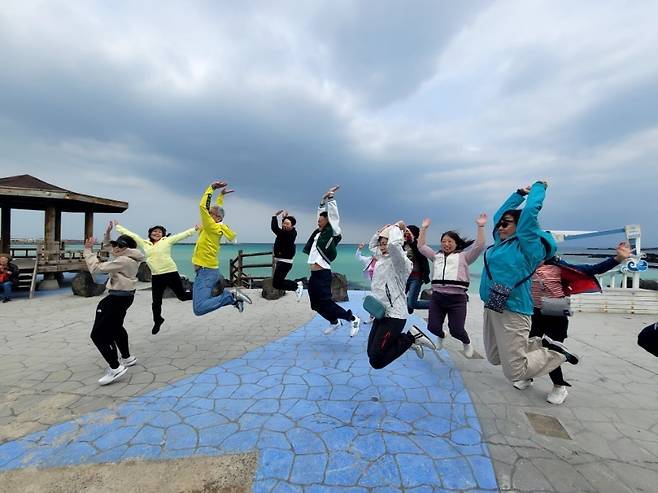 제주 해안 마을을 방문한 홍콩 교장단이 바다를 배경으로 단체 기념 점프를 하고 있다, (제주관광공사 제공)