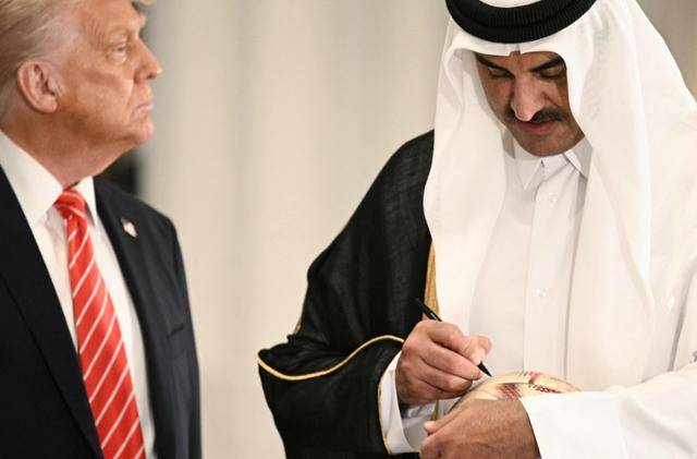 도널드 트럼프(왼쪽) 미국 대통령이 14일 카타르 루사일궁에서 국빈만찬 뒤 축구공에 서명하는 셰이크 타밈 빈 하마드 알사니 카타르 군주(에미르)를 바라보고 있다. 루사일=AFP 연합뉴스