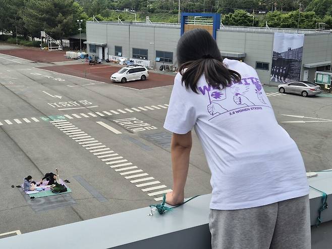 고공농성 500일을 열흘 앞둔 2025년 5월11일, 박정혜씨와 연대하러 온 시민들이 돗자리를 펴고 앉아 손을 흔들자 박정혜씨가 이들을 바라보고 있다. 신다은 기자