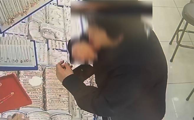 지난달 17일 부산 동구의 한 금은방에서 목걸이를 휴대전화 아래 숨겨 달아난 중년 여성 모습. 업주 제공