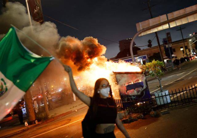 8일 미국 캘리포니아주 로스앤젤레스에서 한 시위 참가자가 멕시코 국기를 들고 불타는 쓰레기통 옆을 지나가고 있다. 로스앤젤레스=AFP 연합뉴스