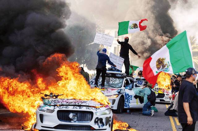 미국 캘리포니아주 로스앤젤레스(LA)에서 8일(현지시간) 자율주행 ‘웨이모’ 택시를 부수고 불을 지른 시위대가 멕시코 국기를 흔들고 있다. AFP연합뉴스