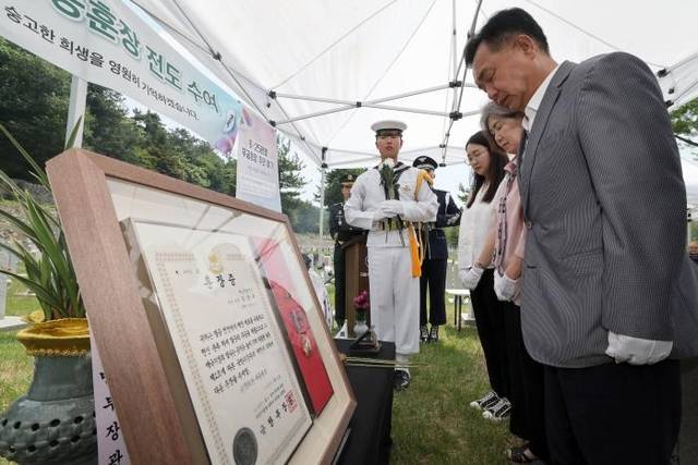 육군인사사령부 6·25무공훈장찾아주기조사단이 9일 국립서울현충원에서 거행한 고(故) 김진수 대위 무공훈장 전도수여식 중 김영철(맨 오른쪽) 씨를 비롯한 유가족이 66년 만에 고인의 묘역을 참배하고 있다. 그 옆으로 주인을 되찾은 금성화랑무공훈장과 훈장증이 보인다. 국방일보 제공