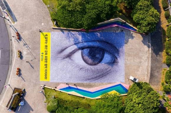 ‘2025 세계환경의 날’이 열리는 제주 국제컨벤션센터에 초대형 ‘눈’이 등장했다. 스위스 예술가 댄 아처(Dan Acher)와 그린피스가 협업한 가로 30m 세로 20m의 #WeAreWatching 깃발로 전 세계 시민 6472명이 자신의 초상을 제공해 만들어졌다. 플뿌리연대 제공