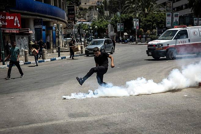10일(현지시각) 서안지구 나블루스 구시가지에서 군사 공습 중 이스라엘군이 최루탄을 발사하자 팔레스타인 청년이 이를 걷어내고 있다. 나블루스/AFP 연합뉴스