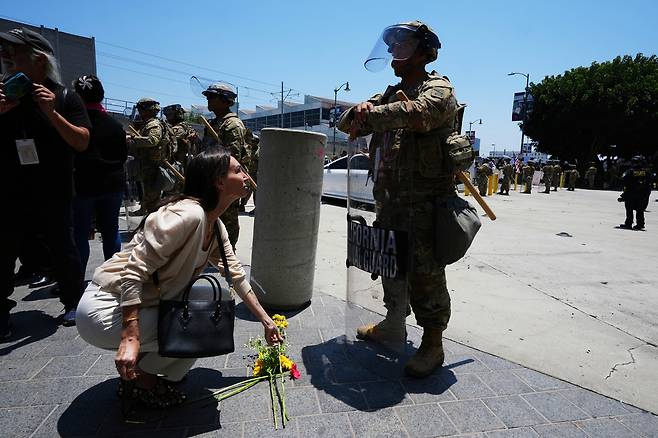 10일 미국 캘리포니아주 로스앤젤레스의 길거리에서 시위대가 모인 가운데 한 여성이 주방위군 앞에 꽃을 놓고 있다. AP연합뉴스