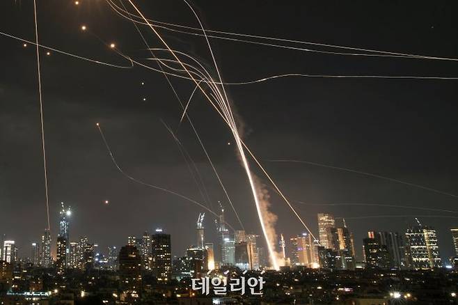 13일(현지 시간) 이스라엘 텔아비브 상공에서 아이언돔 방공 시스템이 미사일을 요격하는 가운데, 발사체가 건물을 강타하고 있다. 이란은 13일 밤과 14일 새벽 탄도미사일 등을 동원해 이스라엘 예루살렘과 텔아비브를 공격했다.ⓒ뉴시스