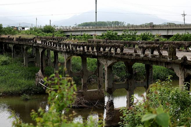강원도 철원군 김화읍 암정리와 용양리를 잇는 암정교(앞쪽). 한국전쟁 당시 폭격으로 일부가 파괴됐고, 전쟁의 상흔을 고스란히 간직한 채 민간인출입통제선 안에 서 있다. 격자무늬 교각이 아치형 난간과 상판을 힘겹게 떠받치고 있다. 다리 곳곳은 무너지고 갈라져 콘크리트와 자갈, 시뻘건 철근이 보인다. 뒤쪽으로 1998년 12월 완공된 제2암정교가 보인다.