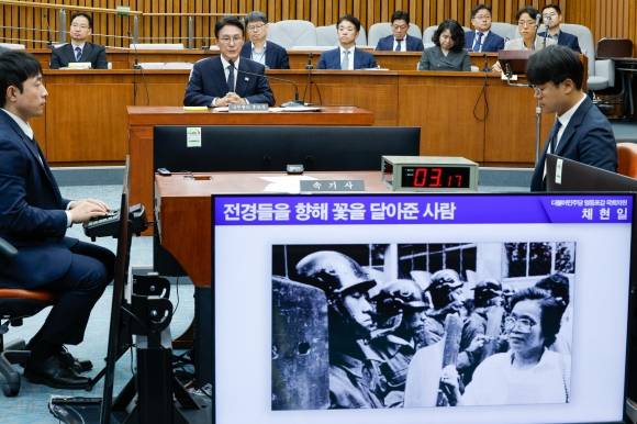 김민석(왼쪽) 국무총리 후보자가 24일 국회에서 열린 인사청문회에서 군사독재 시절 전경들에게 꽃을 달아 주고 있는 어머니 김춘옥 여사 사진이 화면에 등장하자 감정이 복받친 듯 잠시 침묵한 뒤 채현일 더불어민주당 의원의 질의에 답하고 있다. 뉴스1