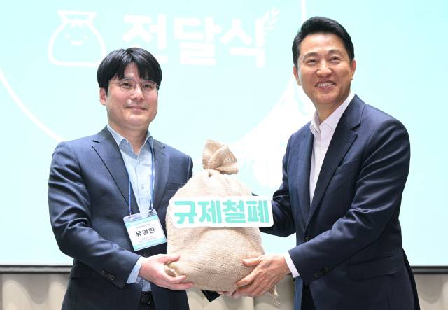 오세훈(오른쪽) 서울시장이 지난달 7일 열린 ‘규제철폐 100일 성과보고회’에서 시민 제안이 담긴 모래주머니를 전달 받고 있다. 사진제공=서울시