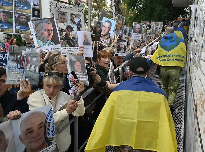 우크라이나 시민들이 26일(현지시각) 북부 체르느히우에서 러시아와의 포로 교환으로 석방된 우크라이나 군인들을 환영하며 실종된 가족의 사진을 들고 있다. 체르느히우/AFP 연합뉴스