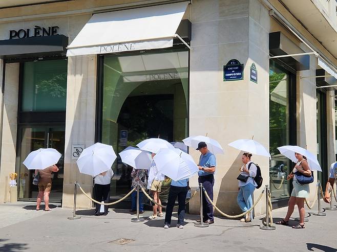 '조금이라도 막아보자' (파리=연합뉴스) 송진원 특파원 = 프랑스 파리 샹젤리제 거리에 있는 한 가방 매장 앞에 손님들이 햇빛 가리기용 우산을 쓰고 대기하고 있다. san@yna.co.kr 2025.06.30.