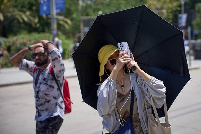 6월 30일 월요일 스페인 바르셀로나에서 한 관광객이 모자와 우산으로 햇빛으로부터 자신을 보호하며 사그라다 파밀리아 교회의 사진을 찍고 있다. 연합뉴스/AP 제공
