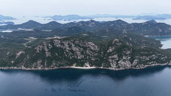 전남 완도 금당도 4산 종주를 하며 사동효종길의 너럭바위에서 동쪽으로 드론을 날려 금당산을 넘겨 사진을 찍었다. 사진 가운데 앞쪽 천길 절벽이 금당산(쟁그랑산)의 부채바위이며 오른쪽 복개산 아래 바위 절벽은 병풍바위로 각각 금당팔경의 제2경과 제1경이다. 그 뒤로 출렁이는 바위 능선은 금당도 5산인 삼랑산 오봉산 봉자산이다. 멀리 조약도(약산도)와 완도 등 다도해가 펼쳐진다.