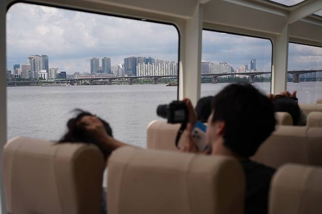A passenger takes out a camera to take Seoul's cityscape ouside the window of Hangang Bus on Tuesday. (Lee Si-jin/The Korea Herald)