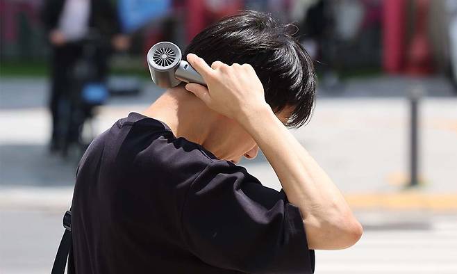 21일 서울 송파구 석촌호수 인근에서 한 시민이 목에 선풍기를 대고 있다. 뉴시스