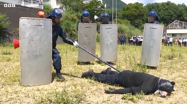 지난 21일 일본 도치기현에서 경찰과 수렵 단체 회원 등이 곰 퇴치 합동 훈련을 진행하는 모습. 경찰이 총에 맞아 쓰러진 곰 역할을 맡은 남성을 막대기로 찔러 반응을 확인하고 있다. /BBC 캡처
