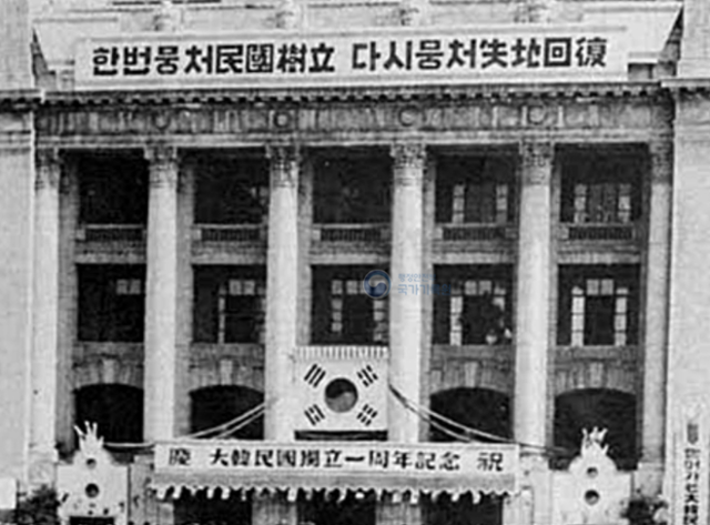 1949년 대한민국 정부 수립 1주년 기념행사 모습. 행사장 건물 상단에 “한번뭉처('뭉쳐'의 당시 표기) 민국수립, 다시뭉처 실지회복”이란 구호가 눈에 띈다. 국가기록원 제공