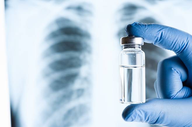한 연구자가 폐 엑스선 사진 앞에서 폐렴 백신 병을 들고 있다. 백신을 맞으면 만성질환자는 65~84%의 예방 효과를 기대할 수 있으며, 미접종자에 비해 치사율이나 중환자실 입원율이 최대 40% 낮아진다는 연구도 있다. 게티이미지뱅크