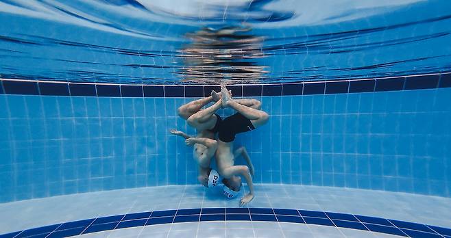 물속에서 연기를 준비하는 SMAT 선수들. 아티스틱스위밍 경기에서는 선수의 신체가 수영장 바닥에 닿으면 감점된다. 선수들은 안정적인 상태를 유지하기 위해 팔과 손으로 물을 밀어내는 스컬이나 양 다리를 회전시키는 에그비터 킥 등의 스킬을 사용한다.