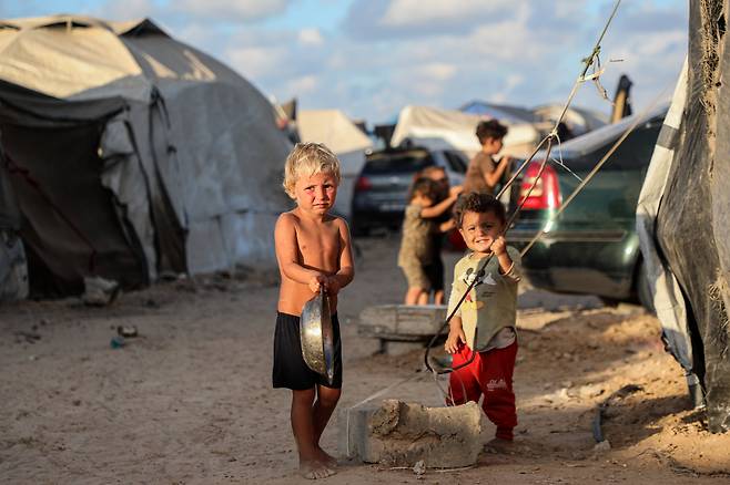 지난달 30일 팔레스타인 가자지구 중부 누세이라트 난민캠프에서 피란민 어린이들이 빈 그릇을 들고 서있다./신화통신 연합뉴스