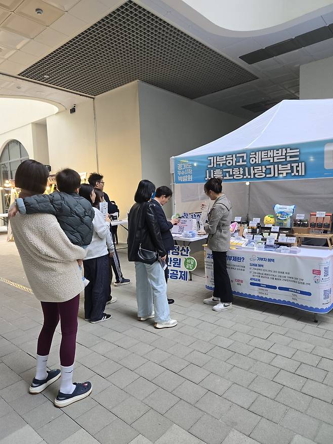 지난 24~25일 시흥시 거북섬 보니타가 광장에서 열린 '2025 경기도 우수시장 박람회'의 시흥시 고향사랑기부제 홍보부스에서 방문객들이 이벤트에 참여하고 있다. <정경아 기자>