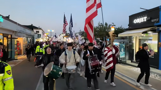 2025 경주 아시아태평양경제협력체(APEC) 정상회의가 열리고 있는 경주의 황리단길에서 보수단체 자유대학이 성조기와 태극기를 들고 ‘윤 어게인’ 사위·행진을 하고 있다. 유튜브 채널 ‘자유드림TV’ 캡처