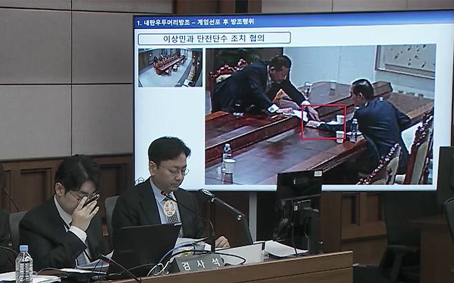 2025년 10월 13일 서울중앙지법 형사합의33부(부장판사 이진관) 심리로 열린 한덕수 전 국무총리 2차 공판에서 특검이 제시한 12·3 비상계엄 당일 대통령실 폐쇄회로(CC)TV 영상 화면에 한 전 총리(오른쪽)와 이상민 전 행정안전부 장관이 계엄 관련 문건을 주고받고 있는 모습이 재생되고 있다. 법원 공판 중계 화면 캡처