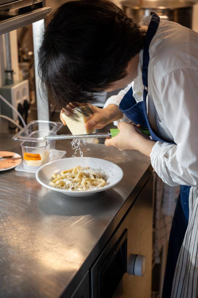 신정원 셰프가 주방에서 파스타 위에 치즈를 갈아 올리고 있다.