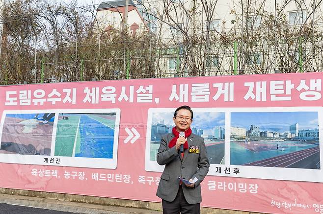 최호권 영등포구청장과 뒤편에는 ‘도림유수지 체육시설, 새롭게 재탄생’이라고 적힌 현수막이 걸려있는 사진이다.현수막에는 개선 전, 후의 육상트랙, 농구장, 배드민턴장, 족구장, 클라이밍장 사진이 나란히 배치되어 있다.