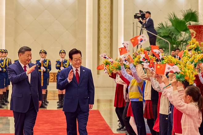 이재명 대통령과 시진핑 중국 국가주석이 지난 5일 베이징 인민대회당에서 열린 정상회담 '공식 환영식'에서 양국 국기를 흔드는 아이들을 향해 인사하고 있다./뉴스1