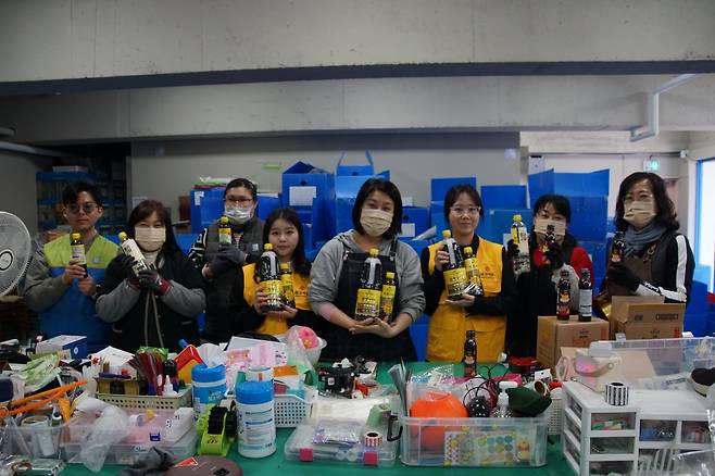 몽고식품 김희영 주임(오른쪽 세 번째)과 예나연 사원(왼쪽 네 번째)이 굿윌스토어 밀알창원1호점 직원들과 함께 기증받은 물품들을 분류하면서 몽고식품 주류 제품들을 들고 기념촬영을 하고 있다.