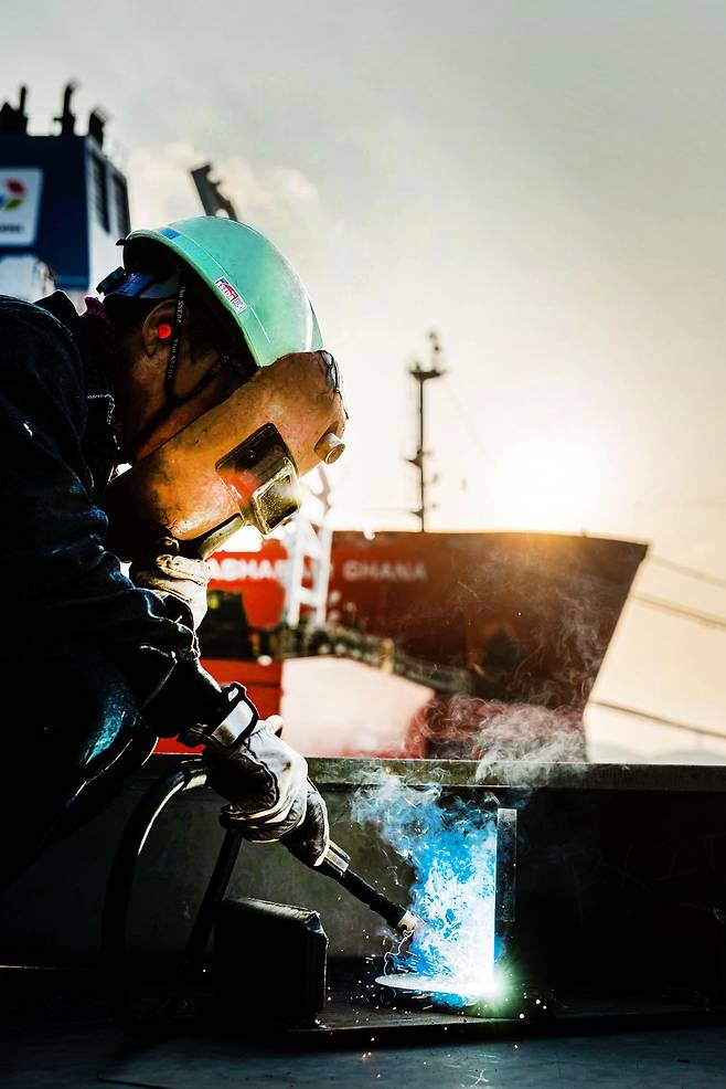 숙련공이 각 손에 용접 마스크와 용접기를 들고 용접을 하고 있는 모습./HD현대중공업